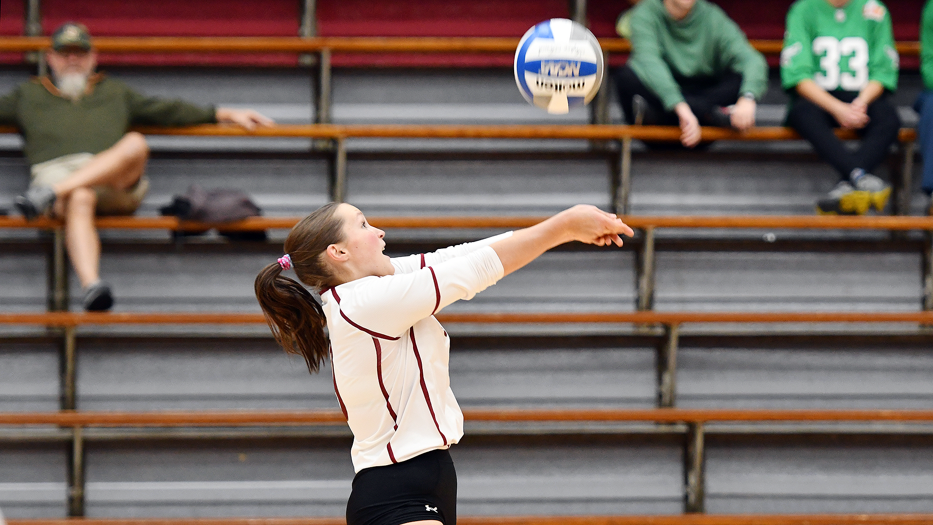 a volleyball player in a white uniform digging the ball as seen from the side