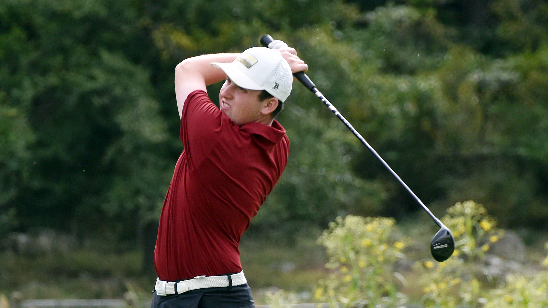a lefty golfer in a red shirt and white hat following through on his swing