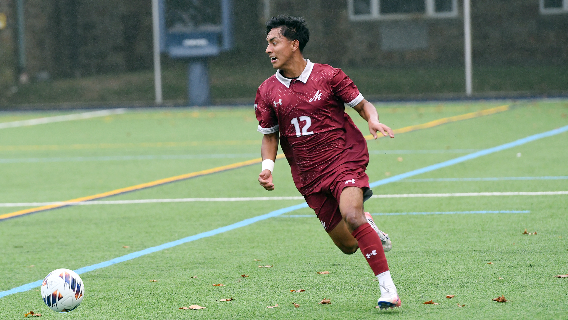 a men's soccer player in a red uniform dribbling to his right on a green turf field