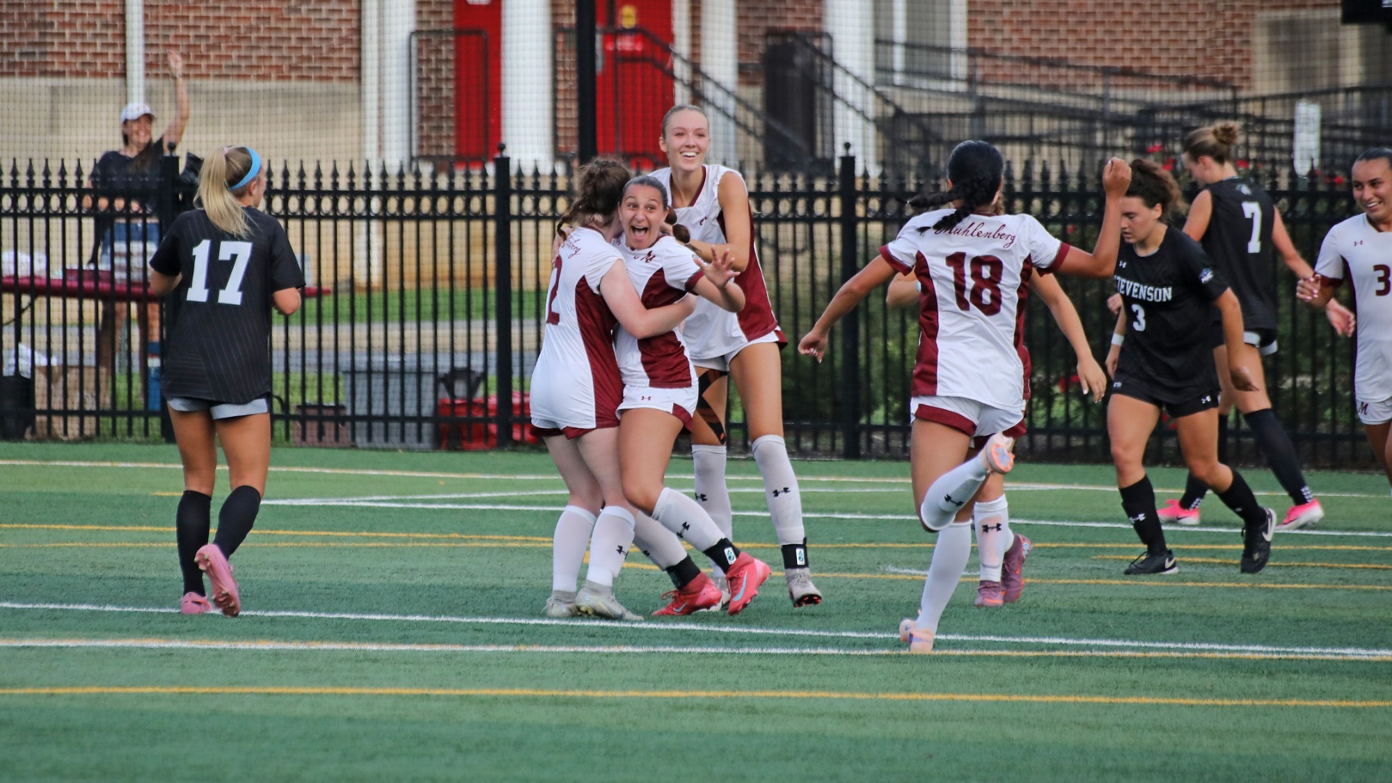 Women's soccer players in white celebrate while opponents in black stand around them