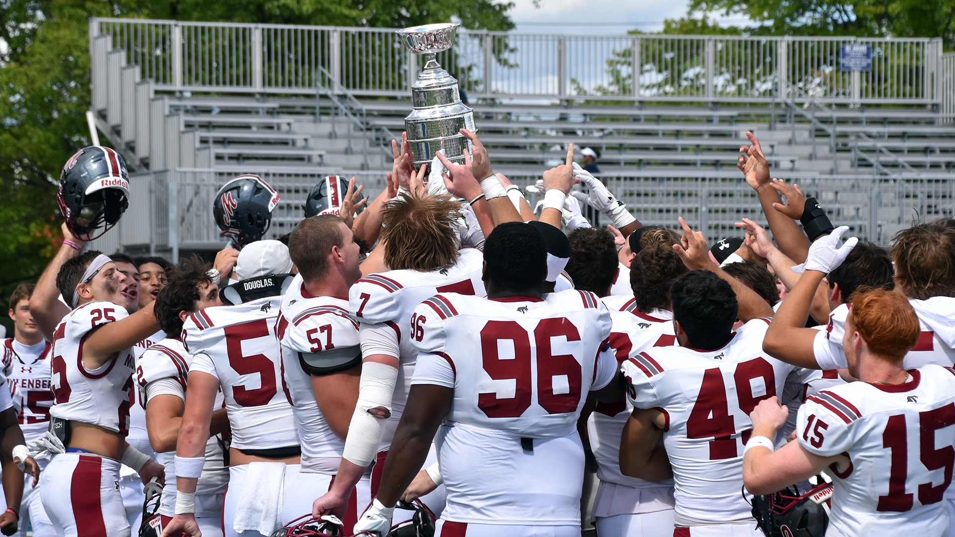 a group of football players in white uniforms raising a silver trophy