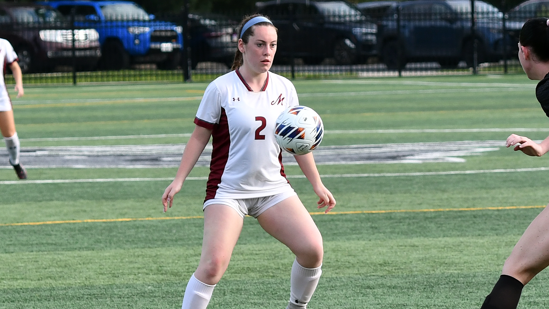 a women's soccer player in a white jersey trapping the ball with her chest on a green turf field