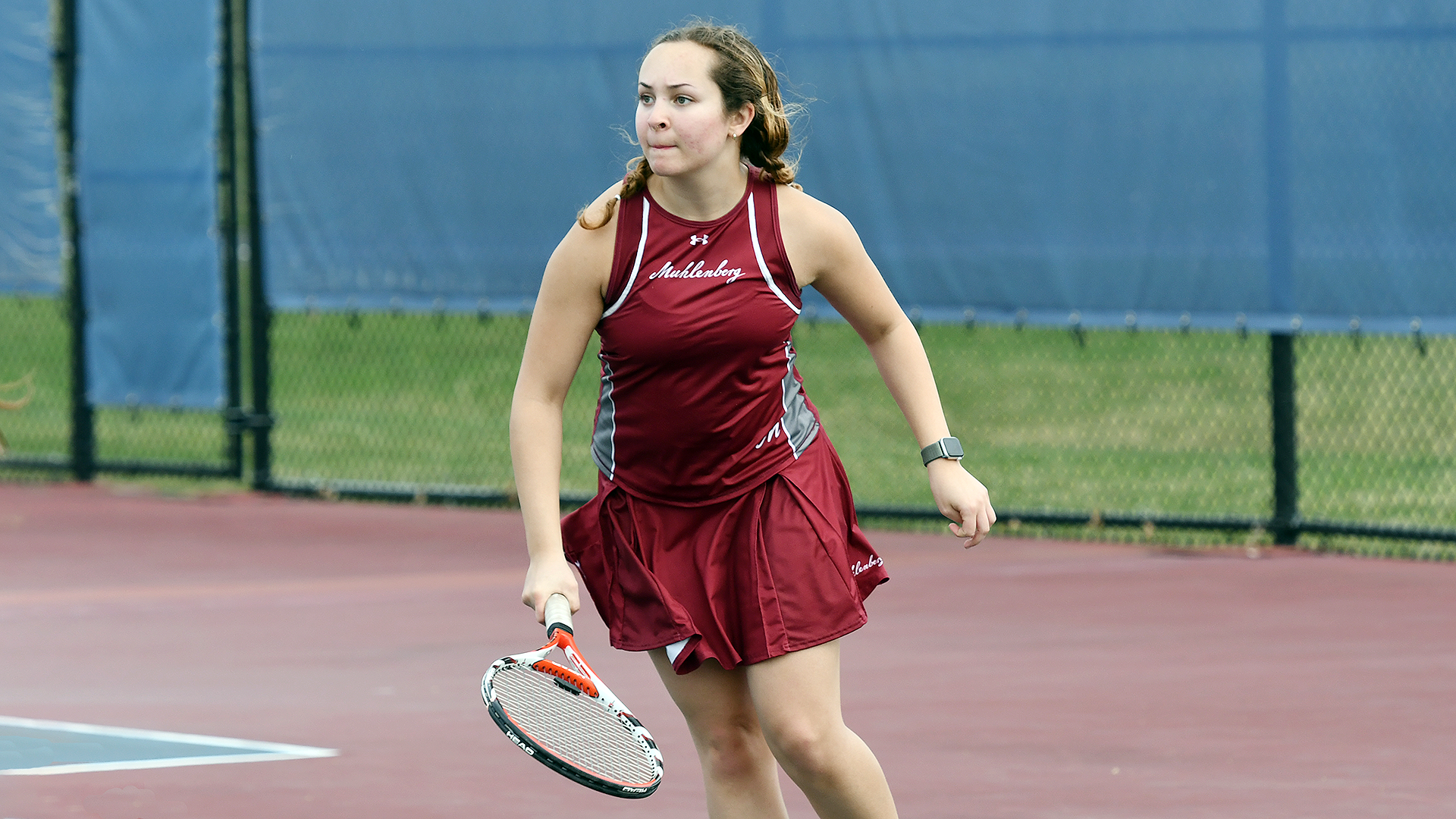 a women's tennis player in a red top and skirt following a shot