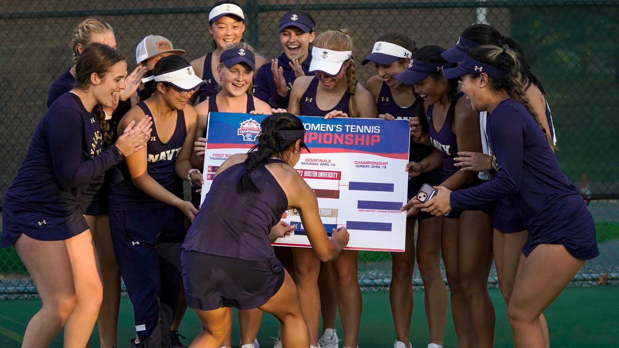 Navy women's tennis team celebrates its Patriot League quarterfinal win on April 17, 2026, as Emma Gu places a navy sticker on the bracket.