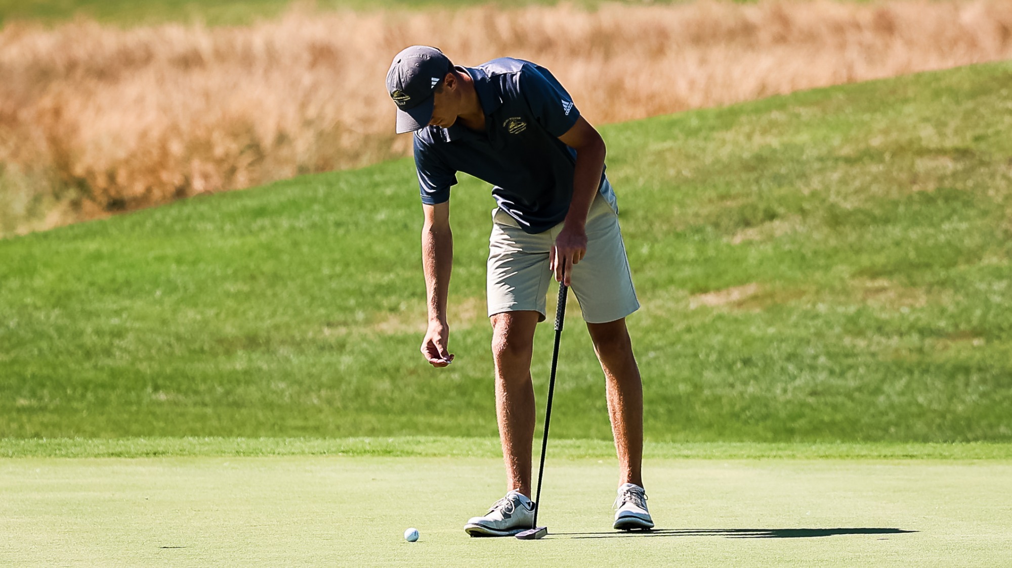 Brayden Schram leans over to pick up his ball out of the the hole