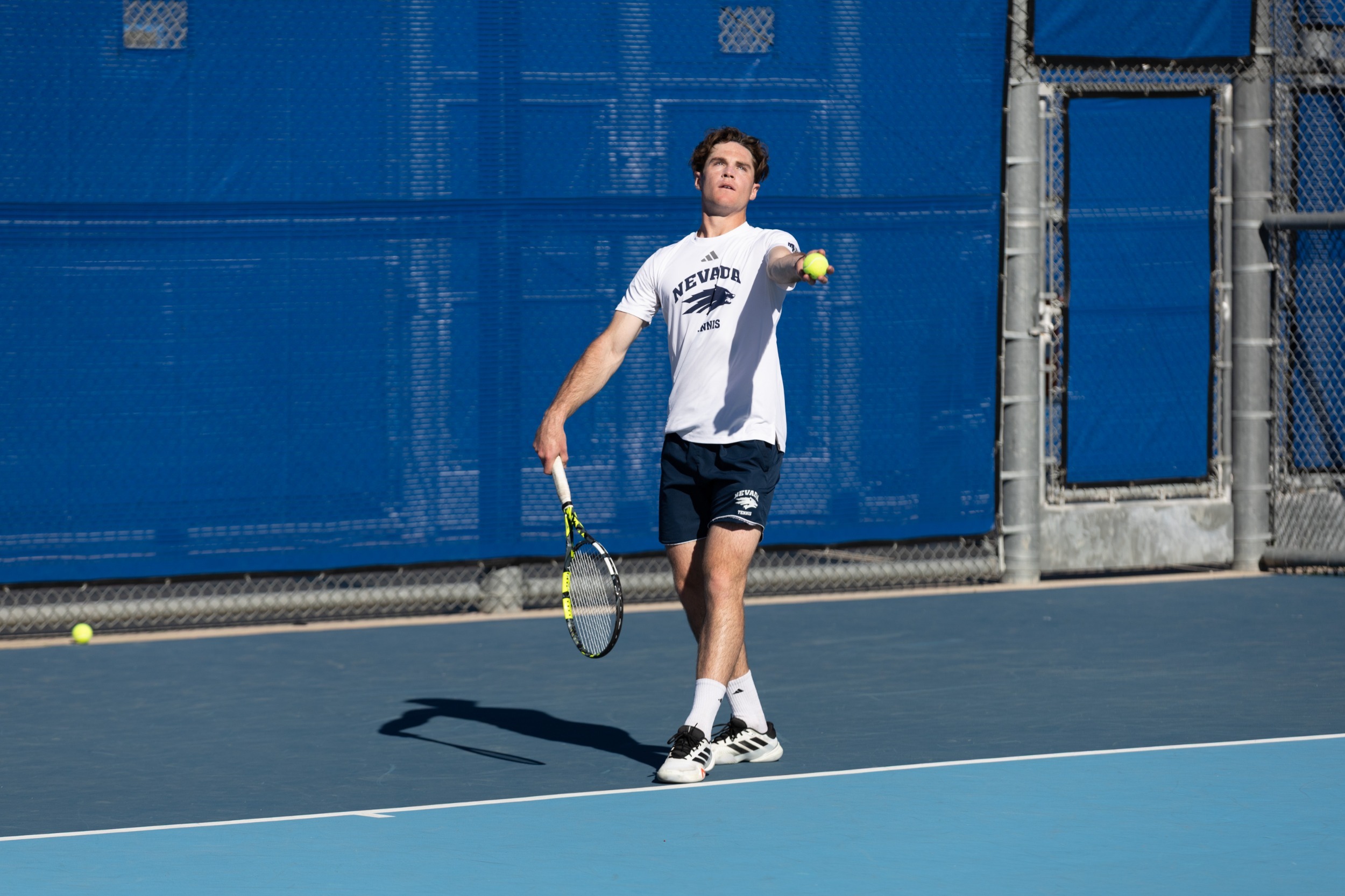 Nevada men's tennis player throws the ball up to serve
