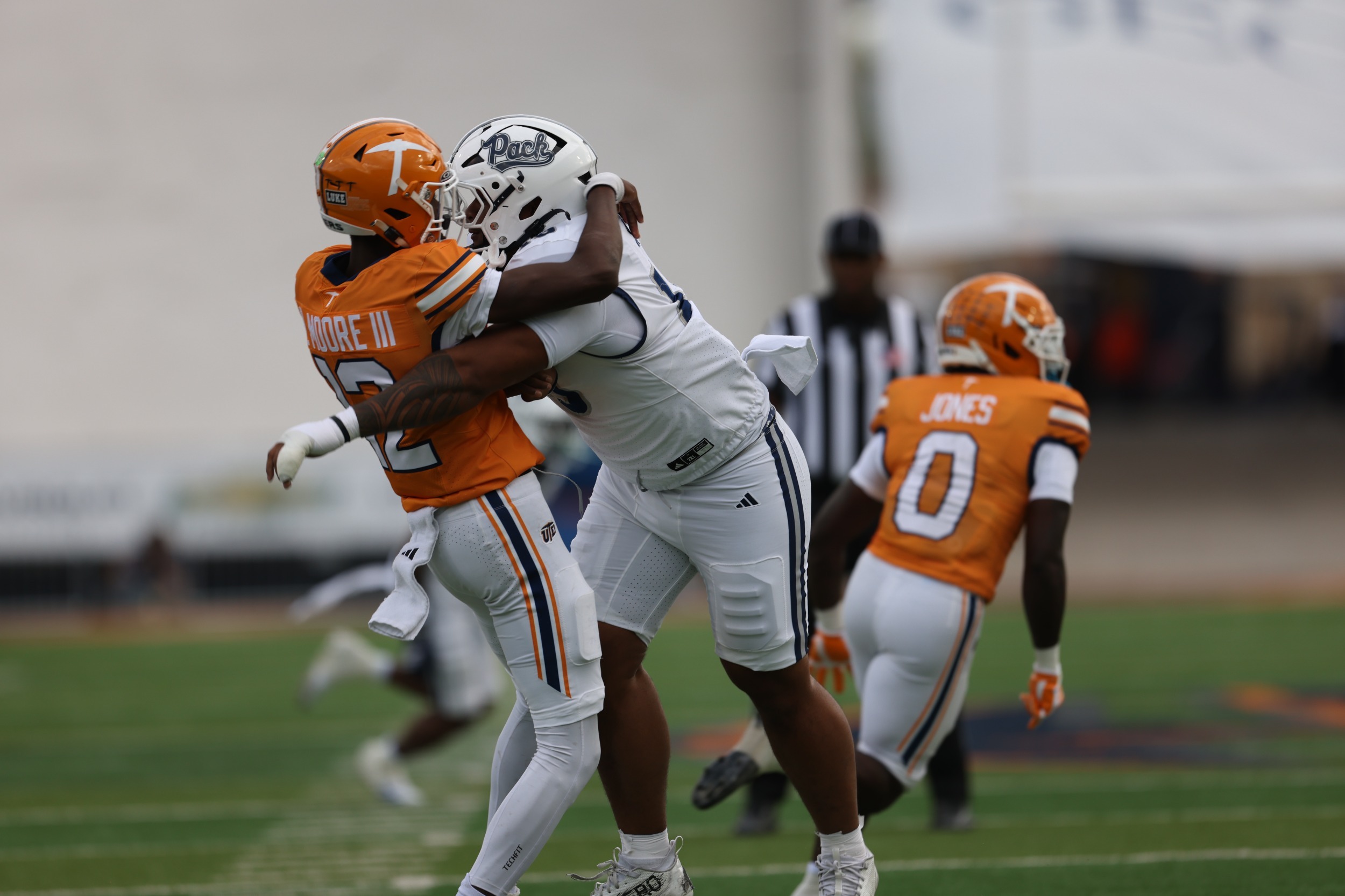 Nevada defender in white jersey tackling UTEP player in orange jersey