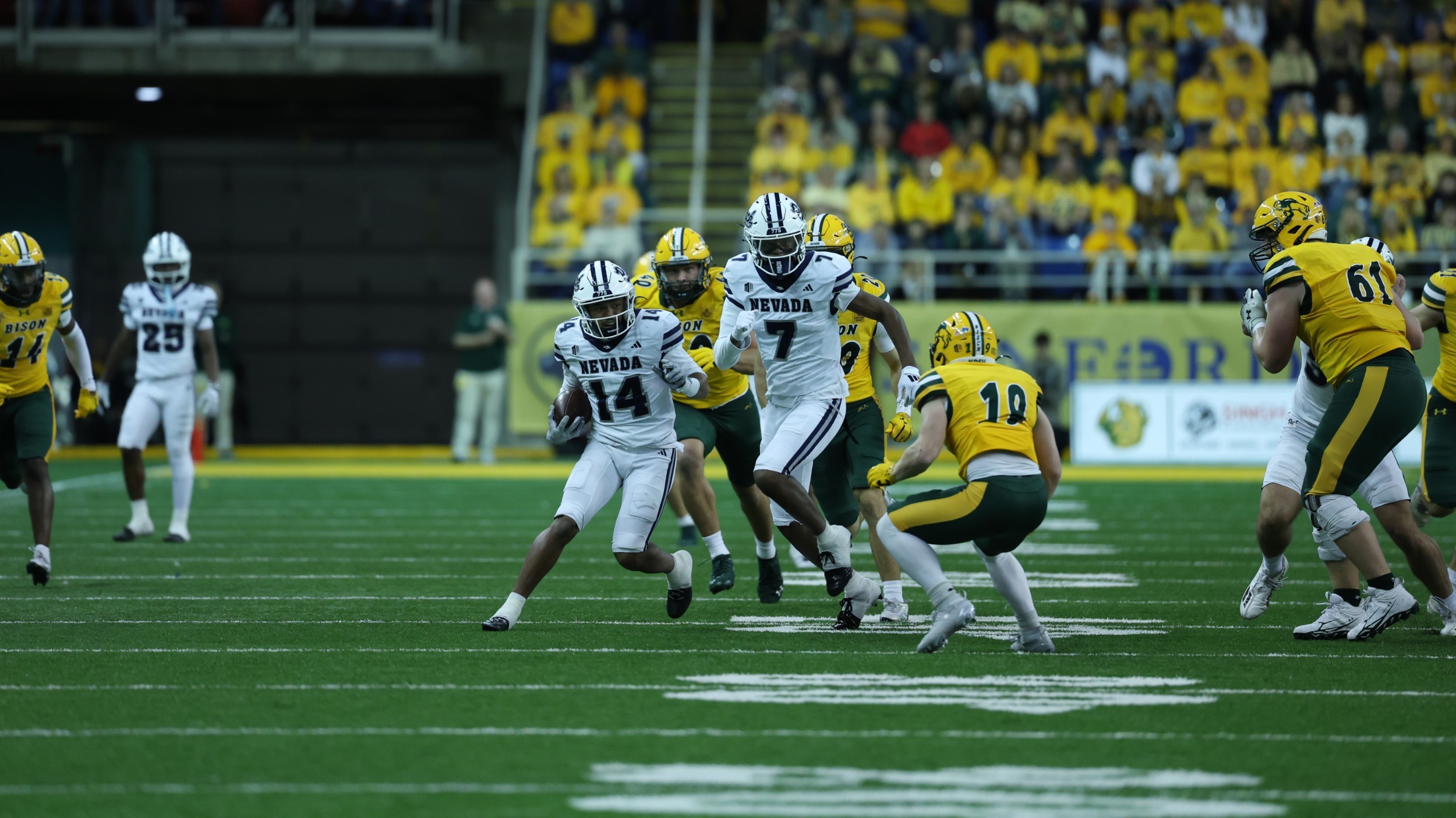 A Nevada player in a light uniform runs with the football at an opposing player