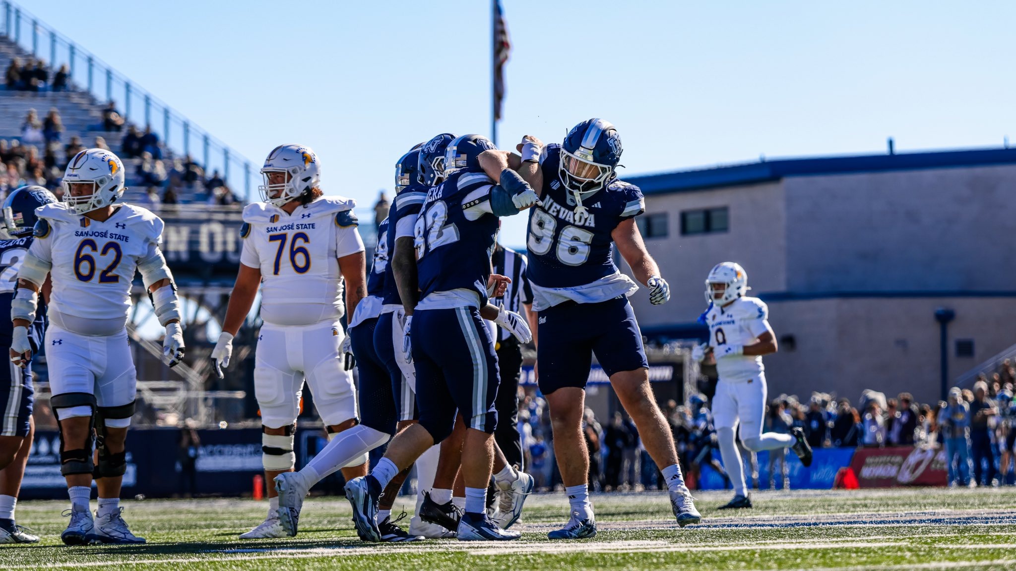 Two Nevada defenders in dark uniforms link arms in celebration after a big play