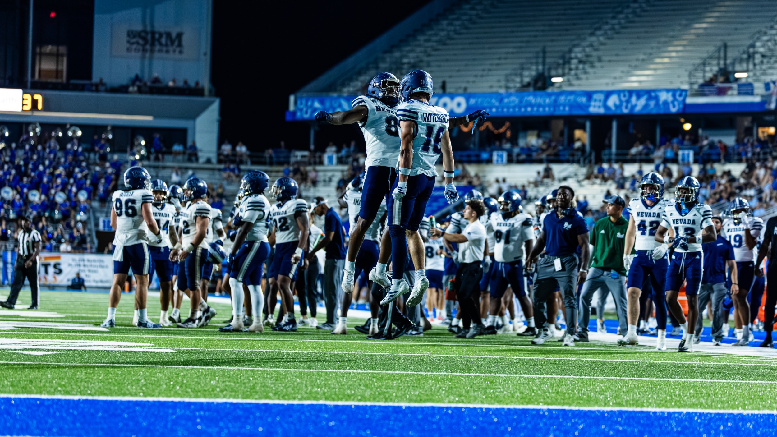 Two Nevada football players jump in the air and chest bump