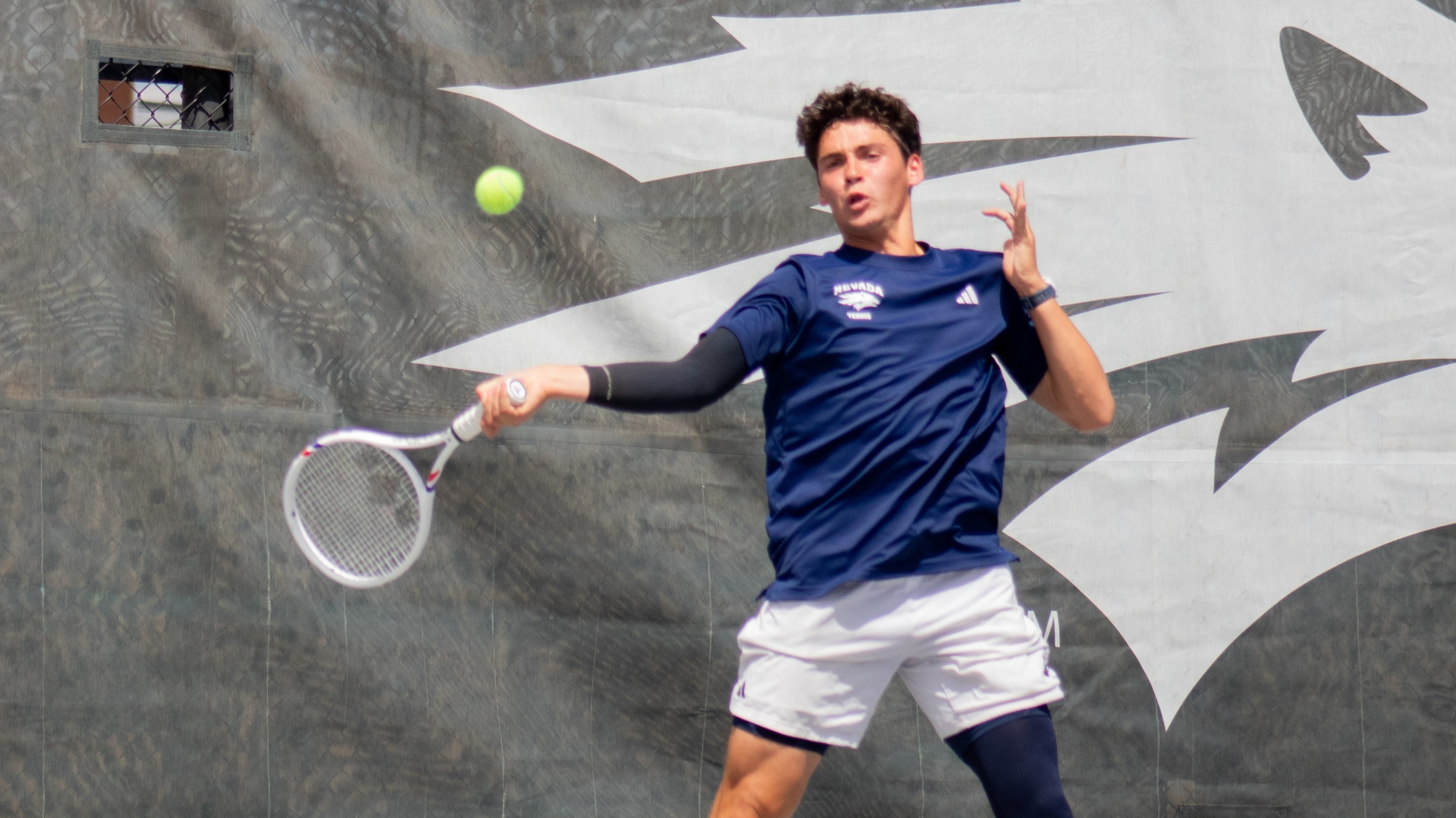 Axel Huysmans in a dark shirt swings a tennis forehand