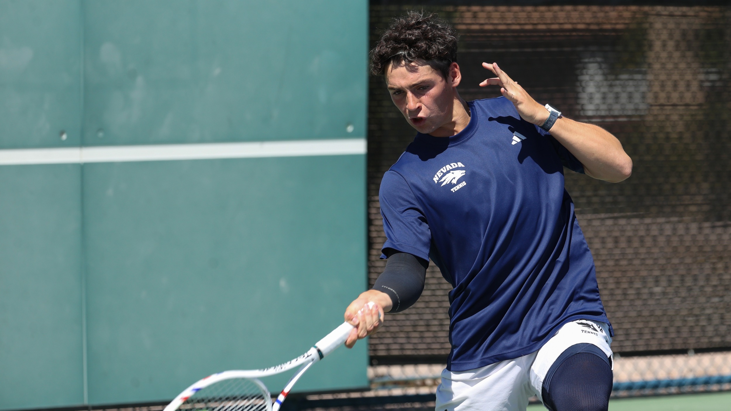 Axel Huysmans in a dark shirt and light shorts swings a tennis forehand
