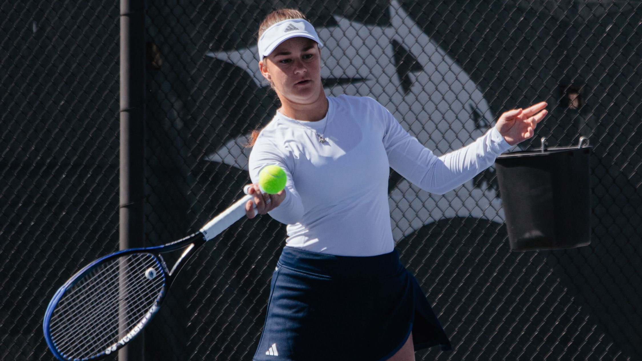 Nevada women's tennis player in a white long-sleeve shirt returns a warmup volley