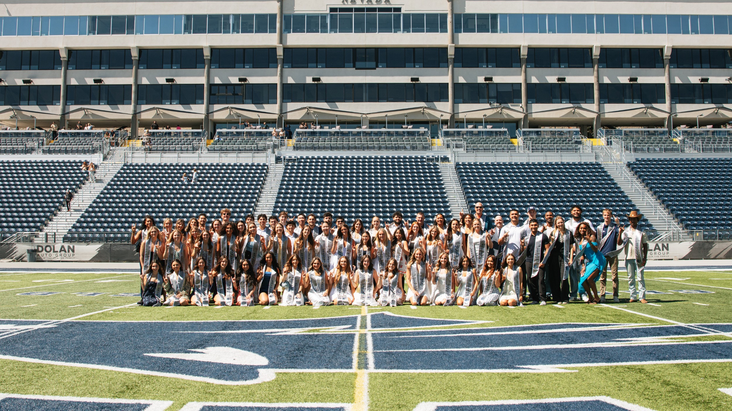 Group of Nevada's 2026 Spring student-athlete graduates posing on the Mackay Stadium turf