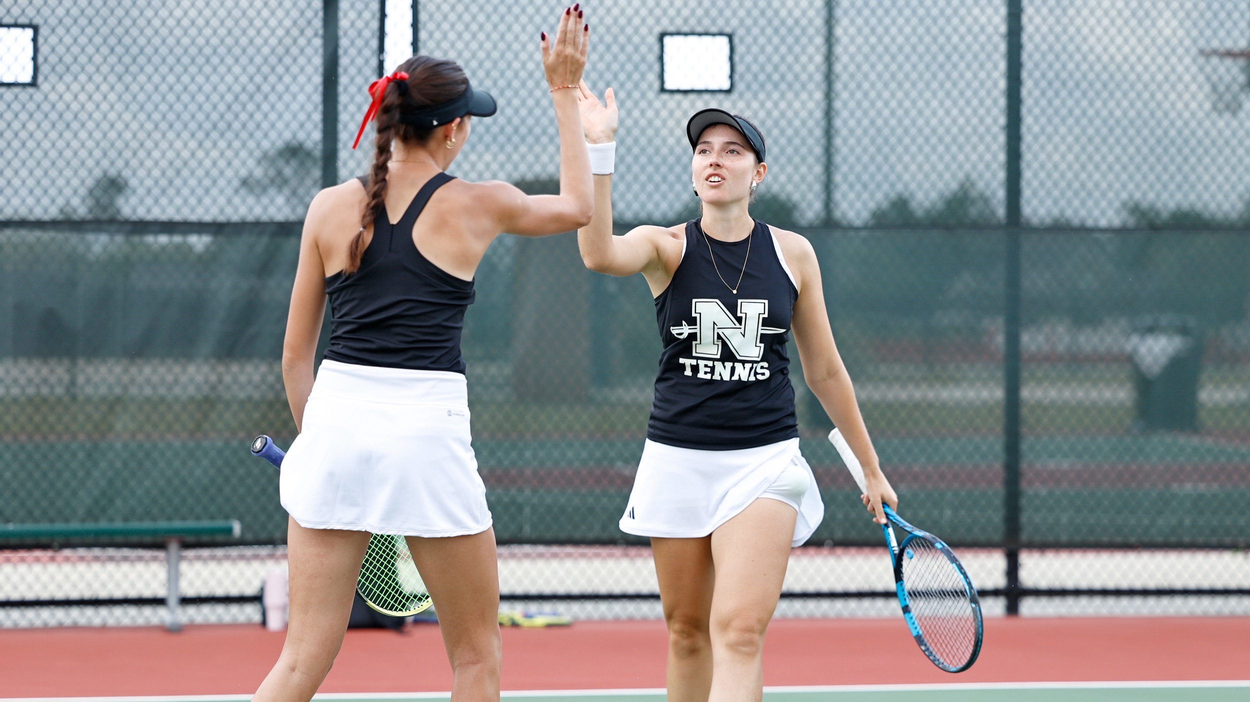 Two Nicholls women's tennis players hi-five after scoring a point