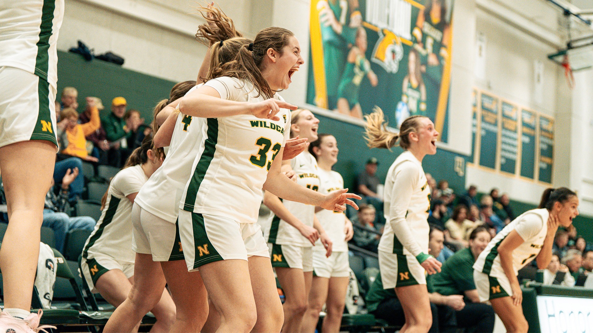 Several women's basketball players celebrate on the bench after a made basket