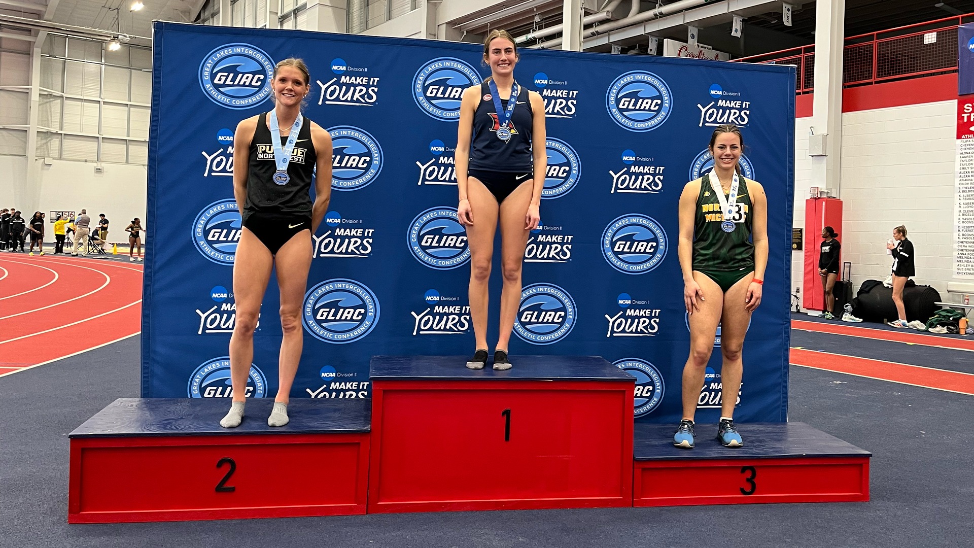 Three track and field participants pose on a podium in front of a GLIAC backdrop