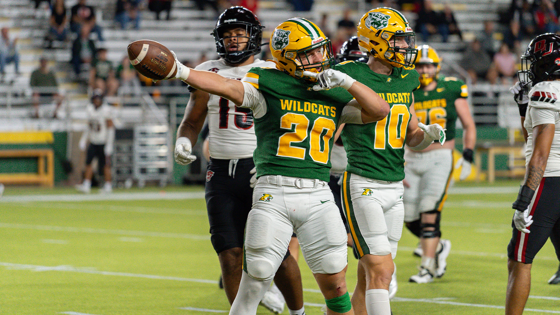 An action shot of a Northern Michigan University football player wearing jersey number 20. He is in a green 