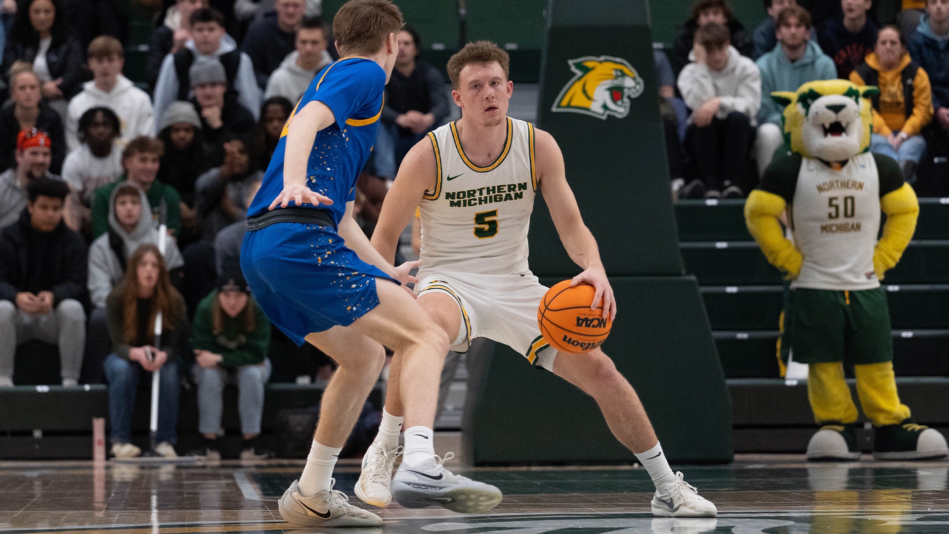 A player in a white #5 jersey dribbles the ball against a defender in a blue jersey