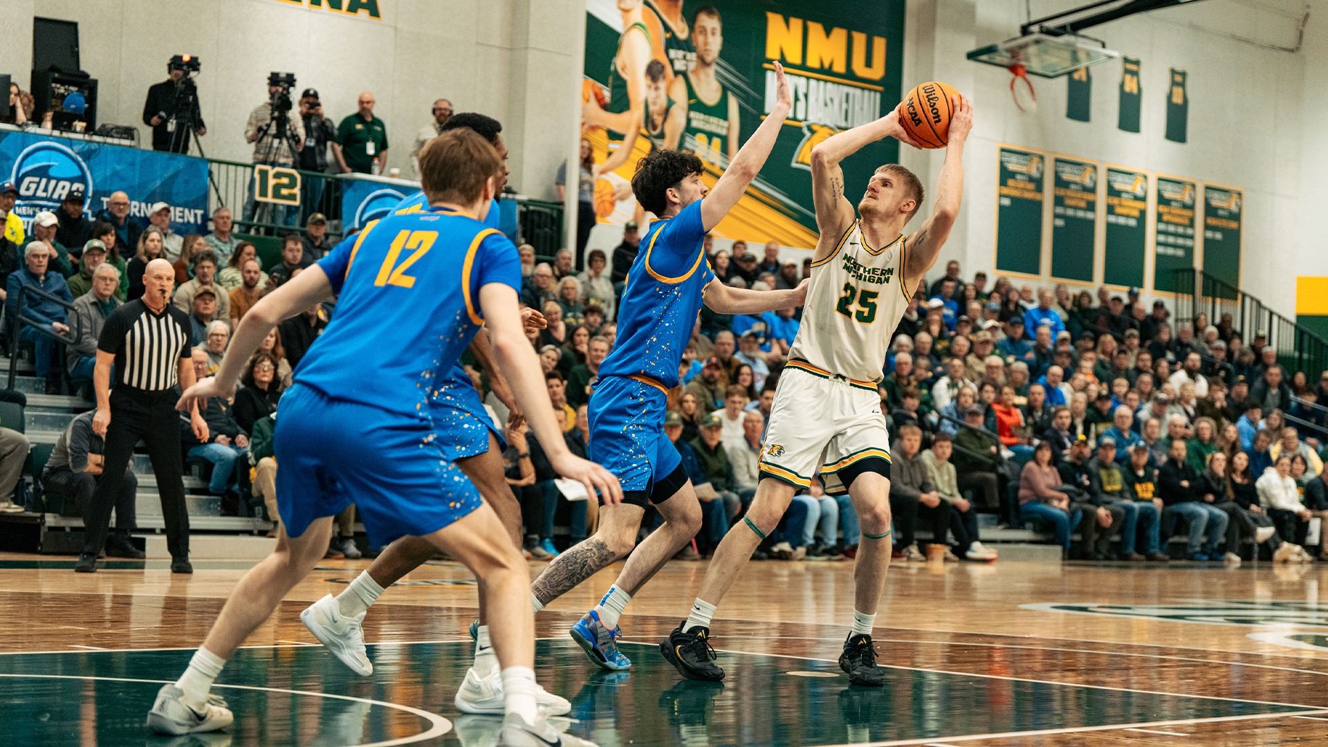 A player in a white #25 jersey goes up for a shot against two defenders in blue jerseys. The fans watch on in the background