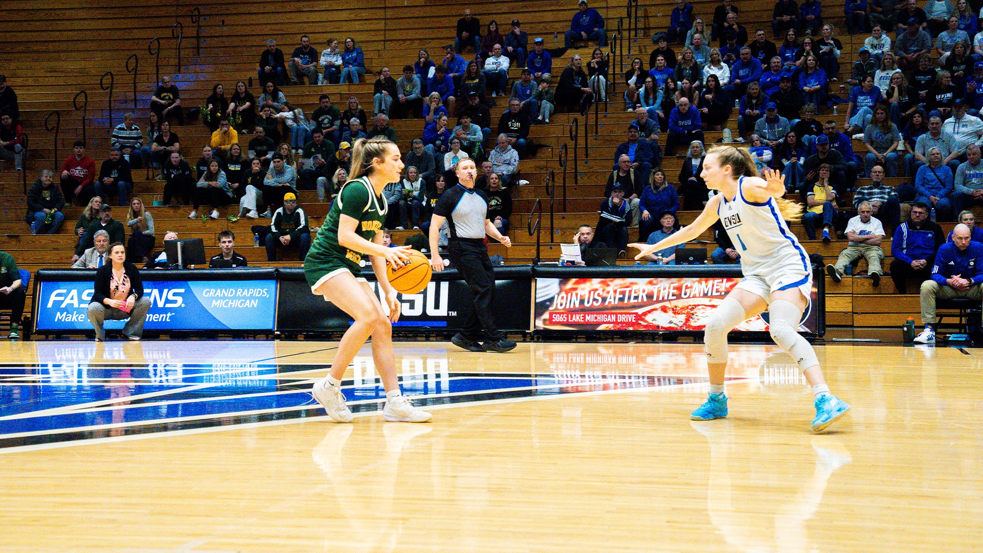 Faith Walder dribbles the ball vs a defender against a dark gym background