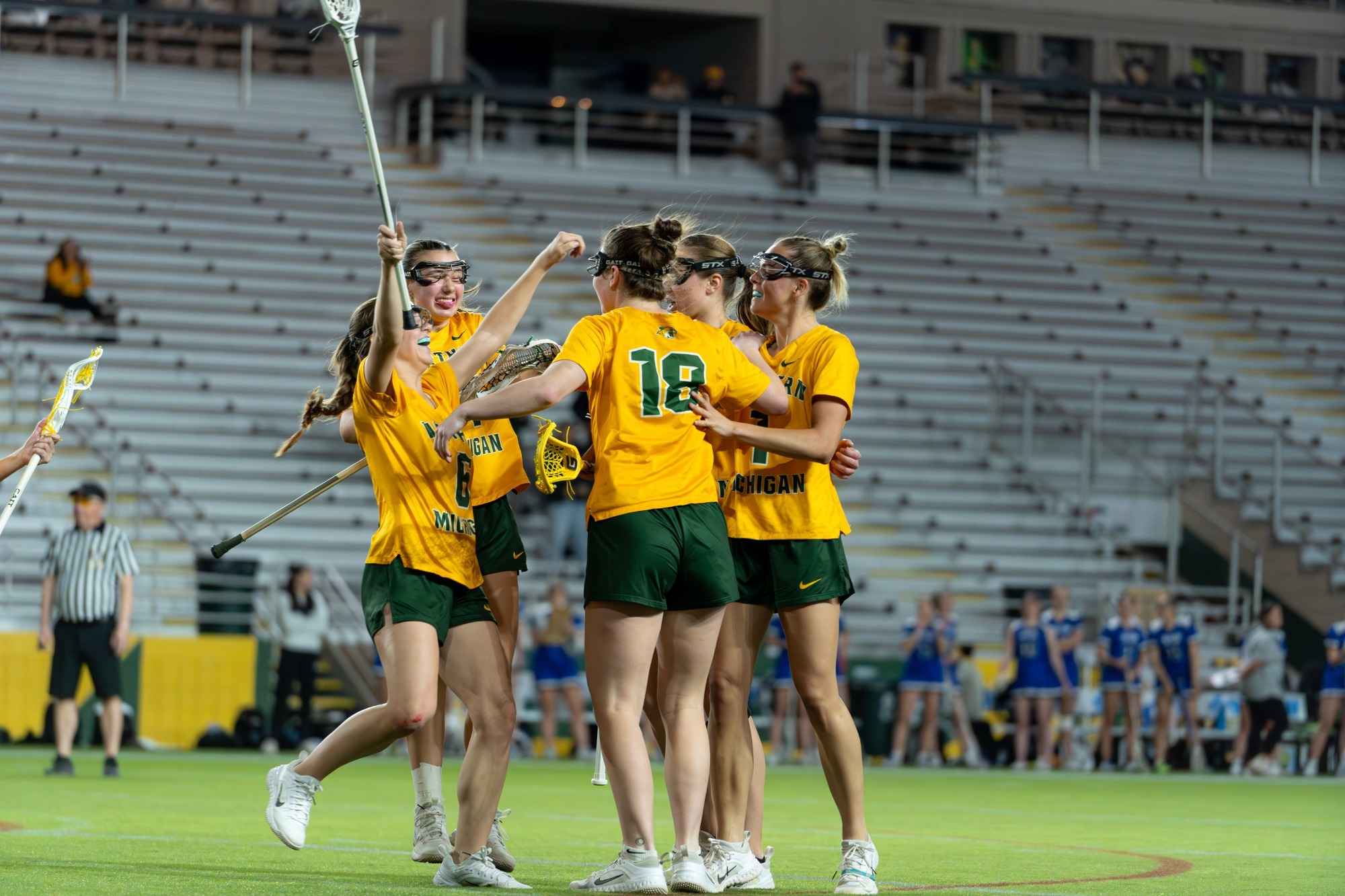 The NMU lacrosse team celebrates scoring a goal, as a group of athletes hug the goal scorer while others run toward the group with their hands held in the air in celebration