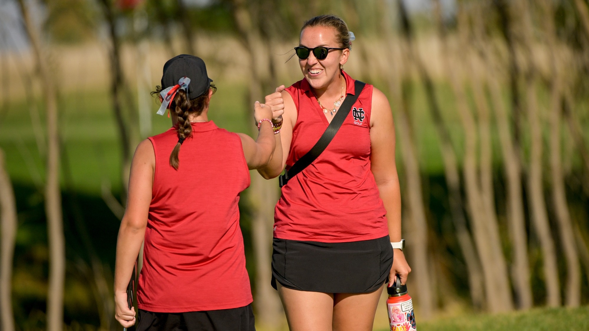 Coach fistbumps her player as she walks back to her golf bag after hitting a nice shot.