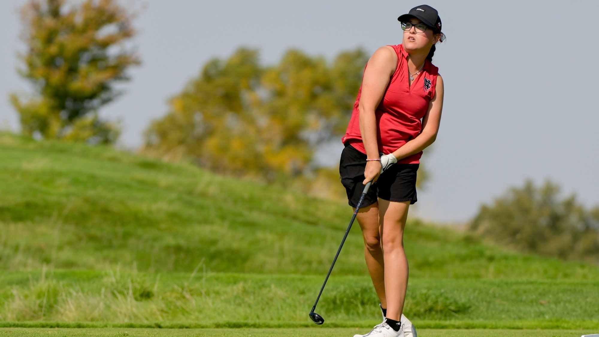 Golfer holds her follow through and watches intently as her shot travels forward.