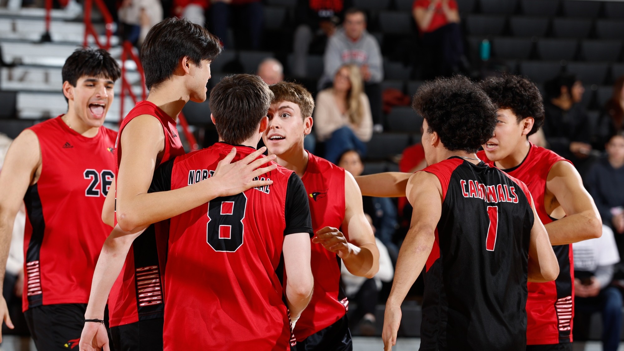 A group of men's volleyball players embrace in a hug after winning a point.