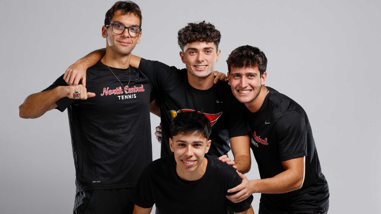 Four men's tennis players place their arms over each other's shoulders and pose for a picture.