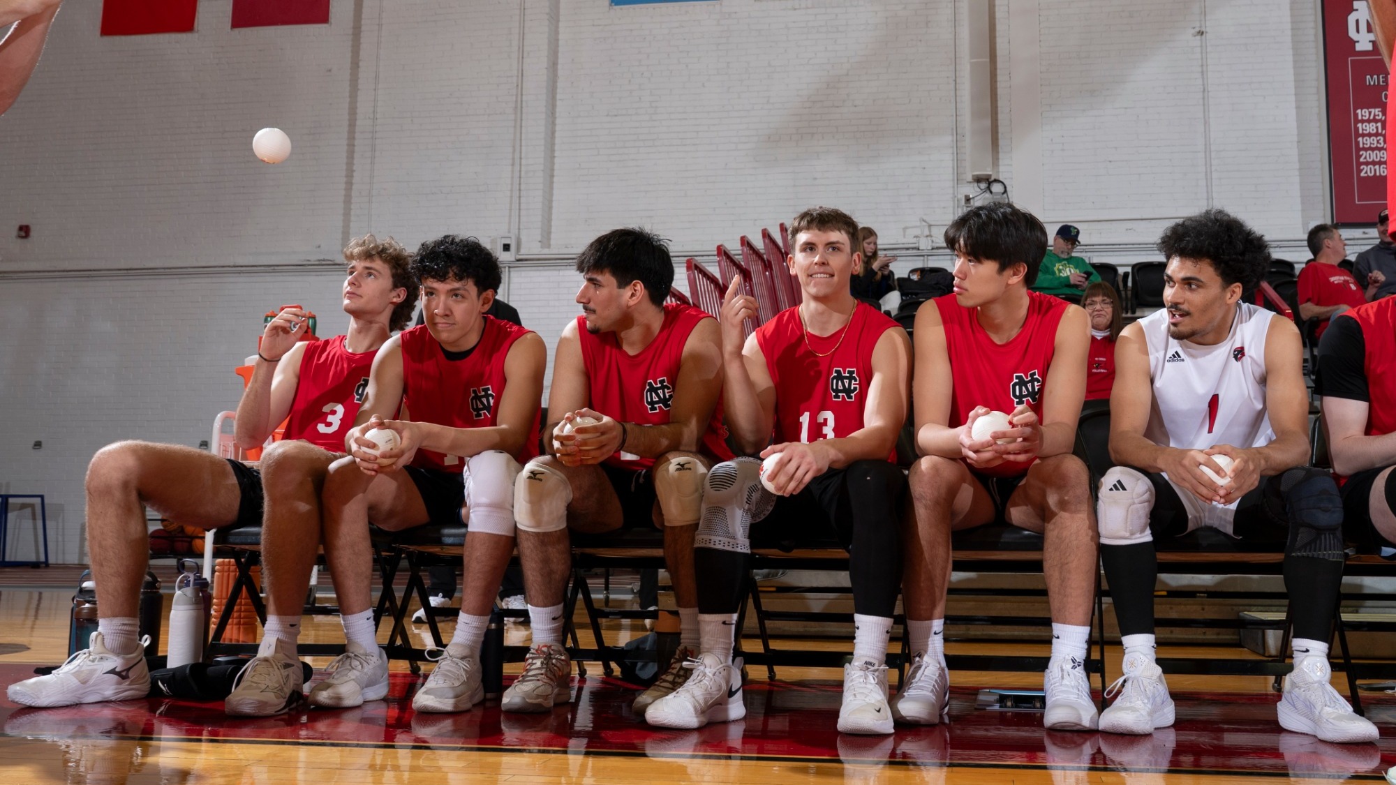 Six Cardinal Men's Volleyball players sit and wait for their names to called during starting lineups prior to a match.