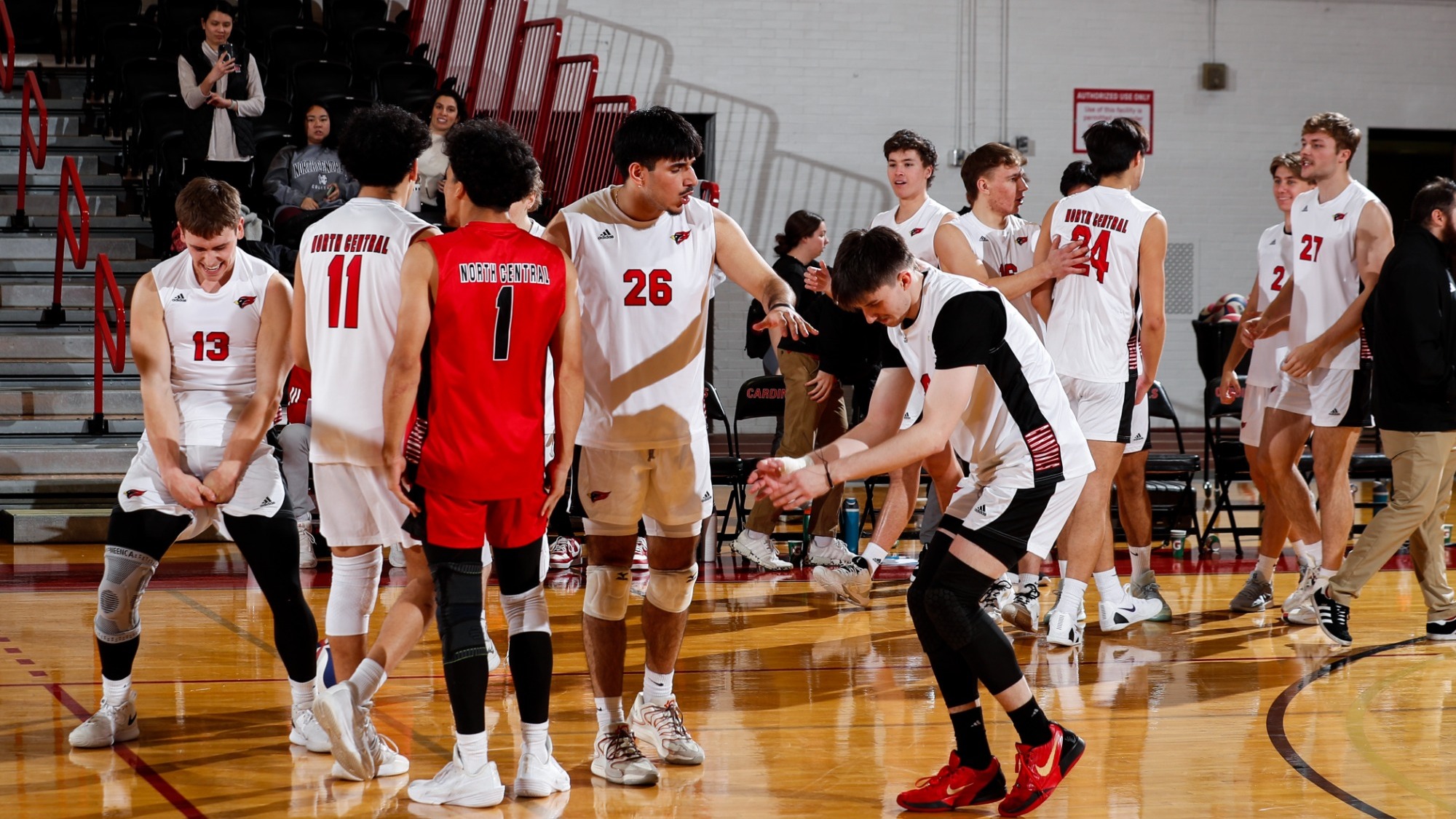 Five men's volleyball players gather to celebrate after scoring a point, huddling together and making different gestures in celebration.