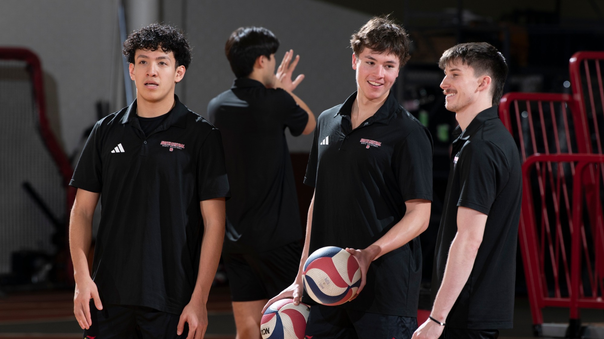 Three men's volleyball players smile at one another before a match.