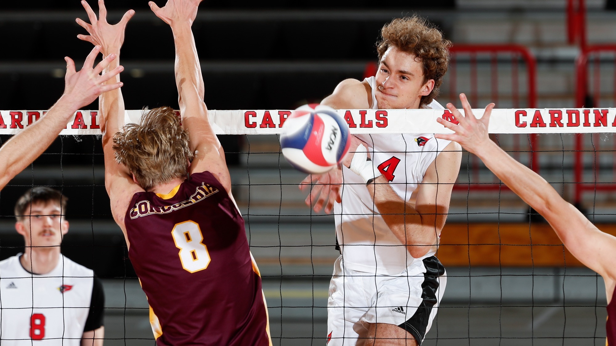 Connor Davis follows through after an attack attempt from the front row during a volleyball match while a defender tries to block it with outstretched arms.