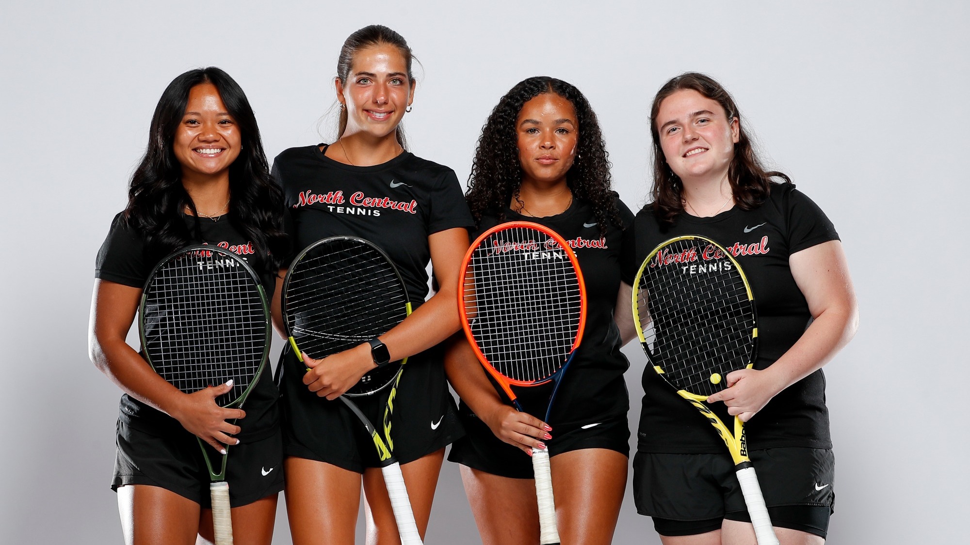 Women's Tennis Seniors pose five across smiling with their rackets in front of a white background.