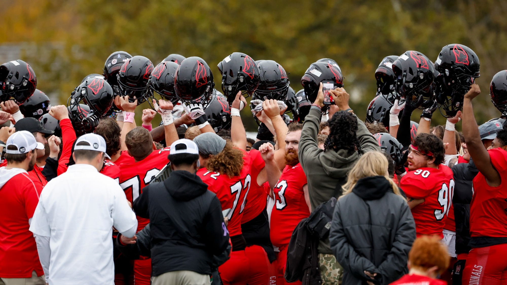 2025 NCC Football Team in a huddle with their helmets hoisted