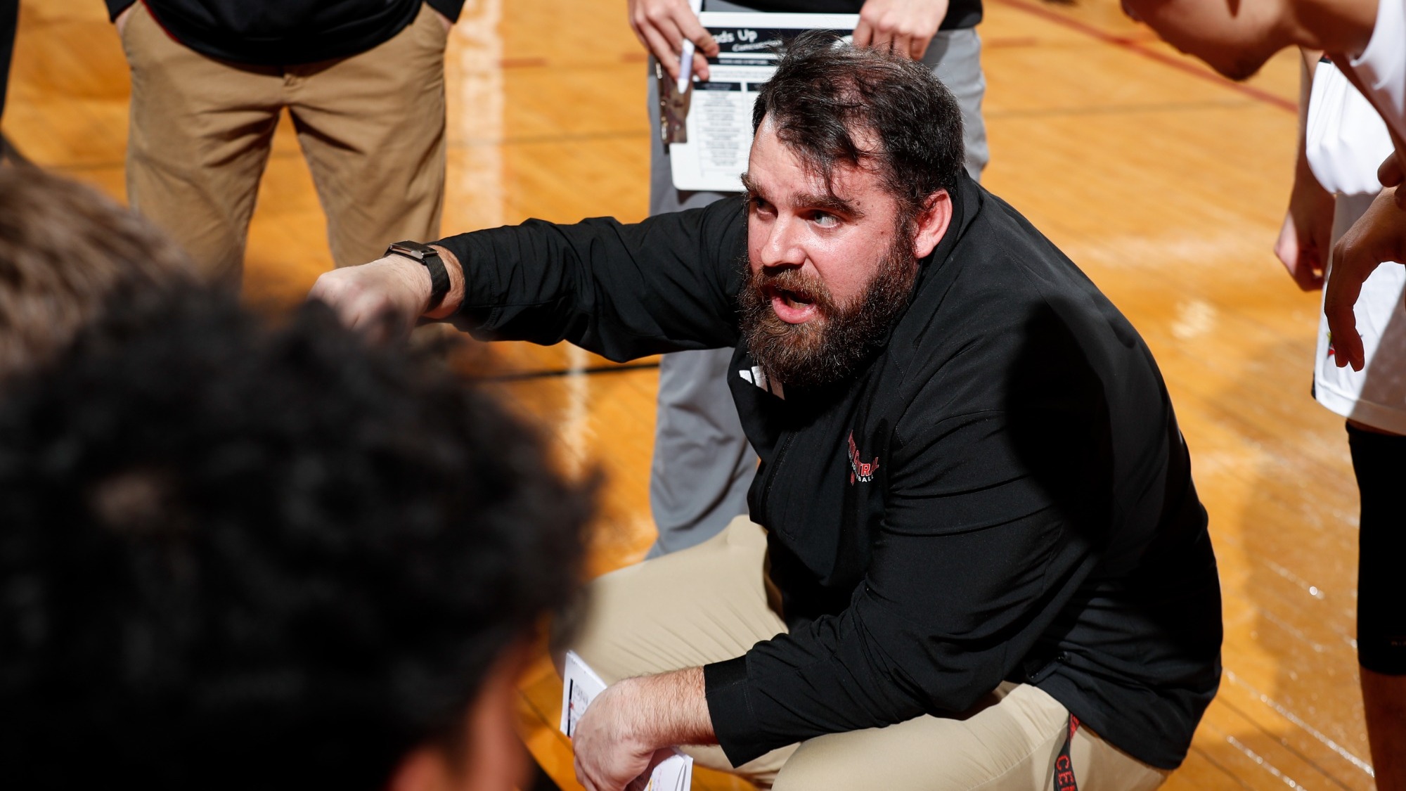 Kevin Kustura squats in the middle of a team huddle, giving instruction to his players during a timeout in a match