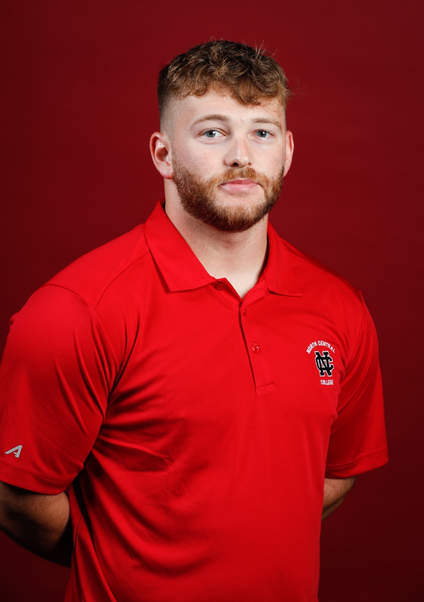 Jake Anderson smiles in front of a red background
