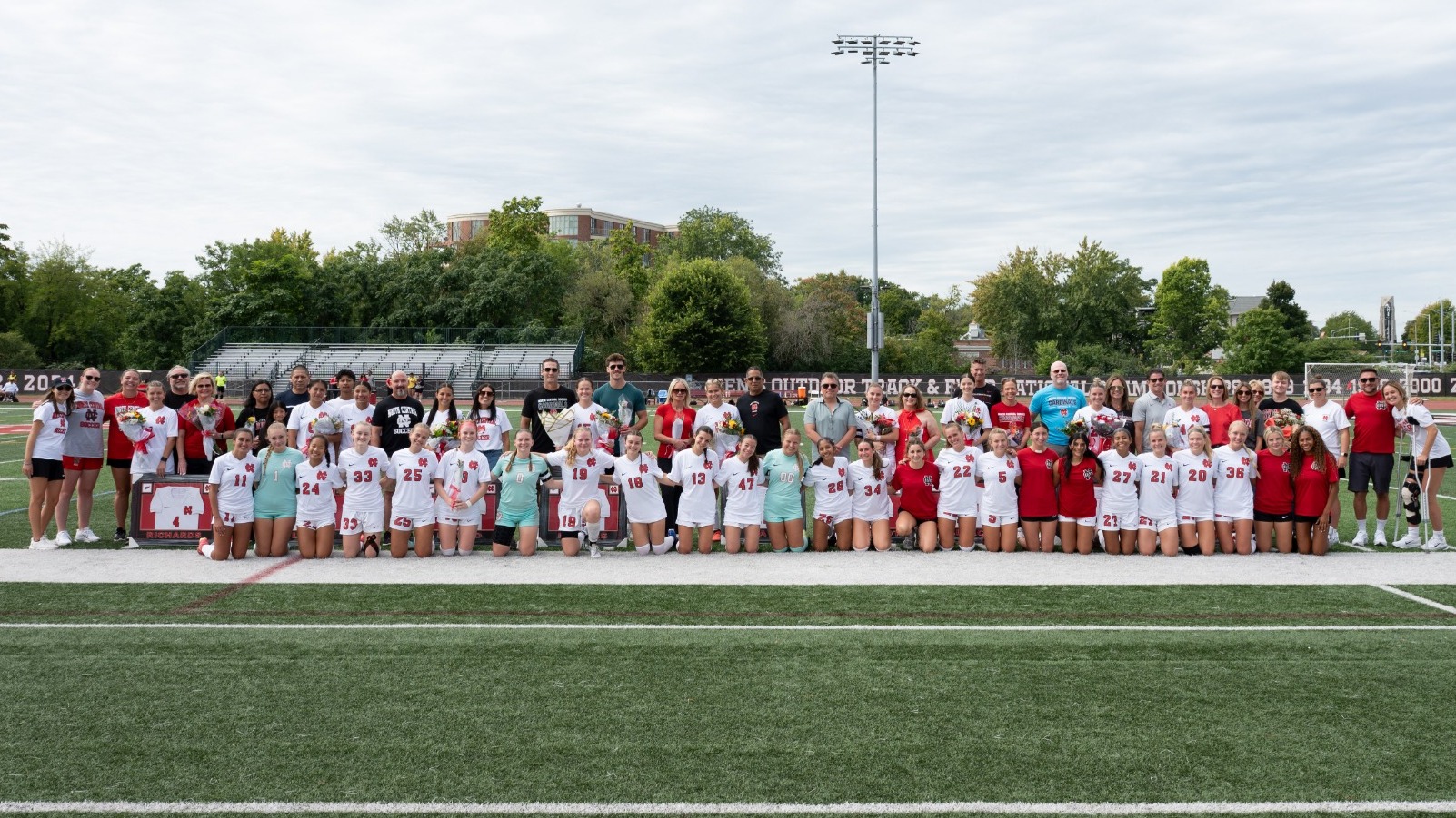 The North Central Women's Soccer team poses while nine student-athletes, all seniors, display jerseys gifted to them during the Senior Day ceremony.