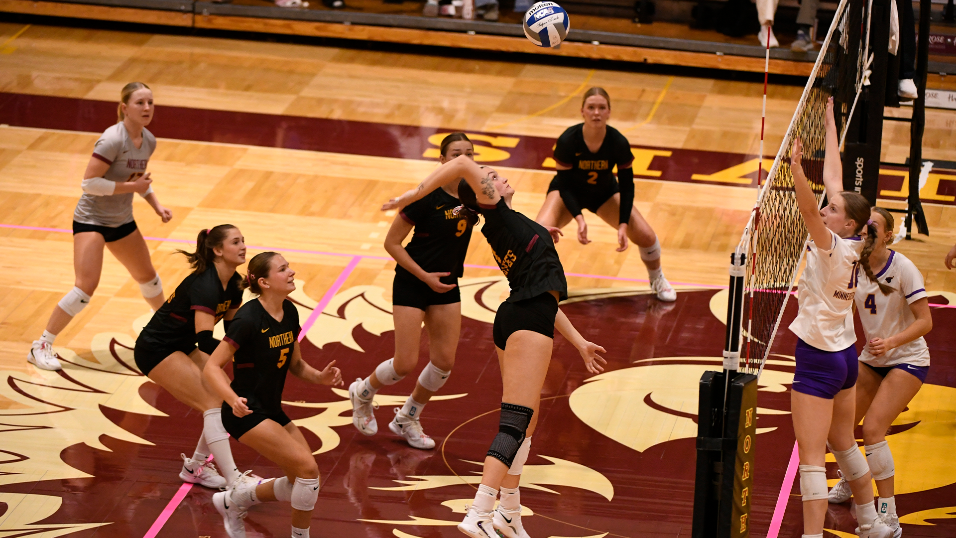 10.17 Volleyball Recap - Victoria Persha attacks the ball mid-air as her teammates watch. MSU Mankato players jump at the net for the block attempt.