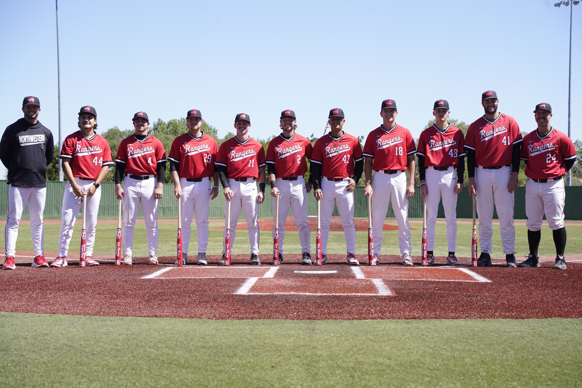 All nine Northwestern baseball seniors stand while holding bats during the senior day ceremony.