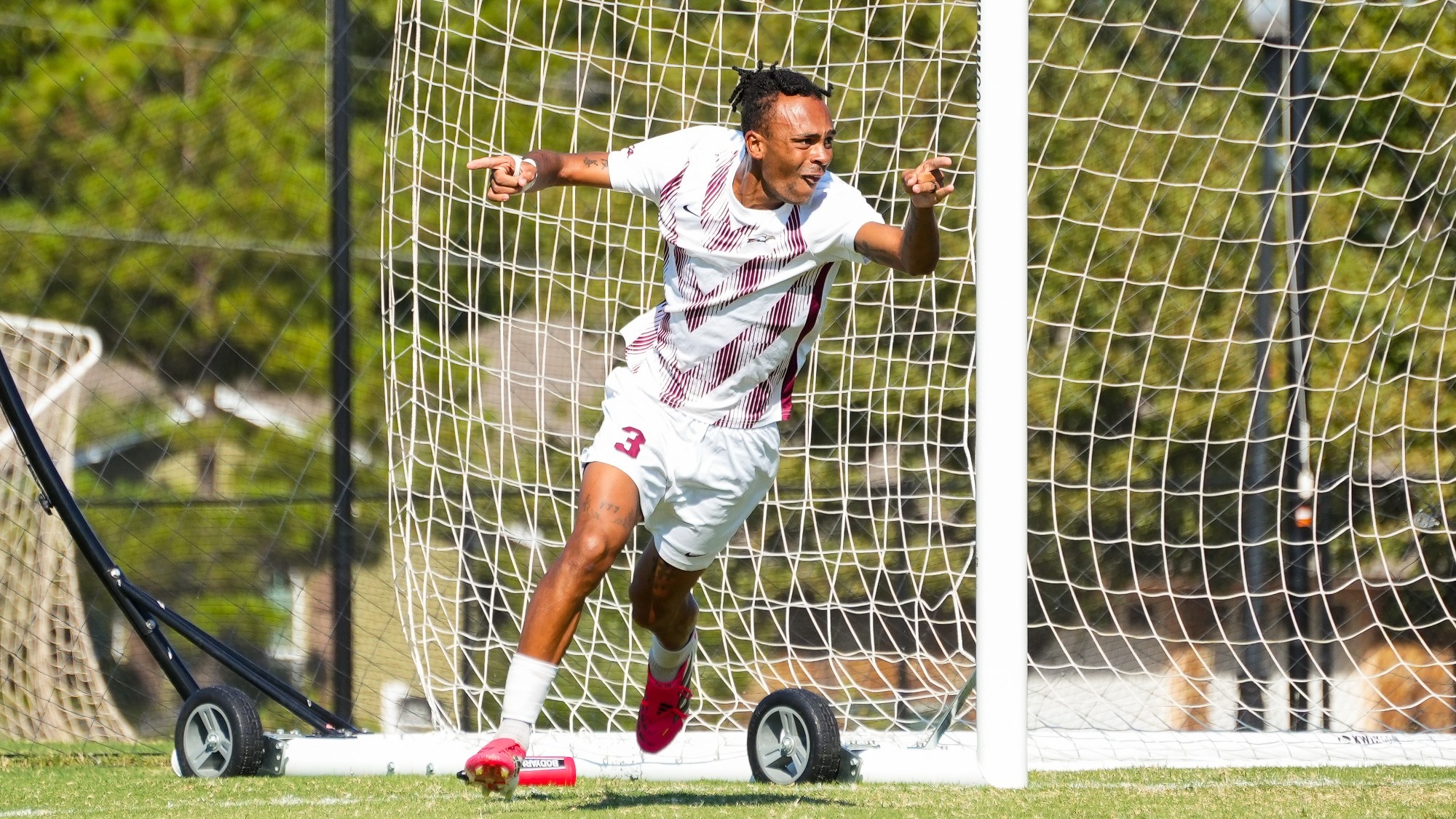 Tyler Ackah-Wheatcroft celebrates scoring a goal, pumping his fist, sprinting while wear a white uniform with maroon chevron pattern, numbers and word marks