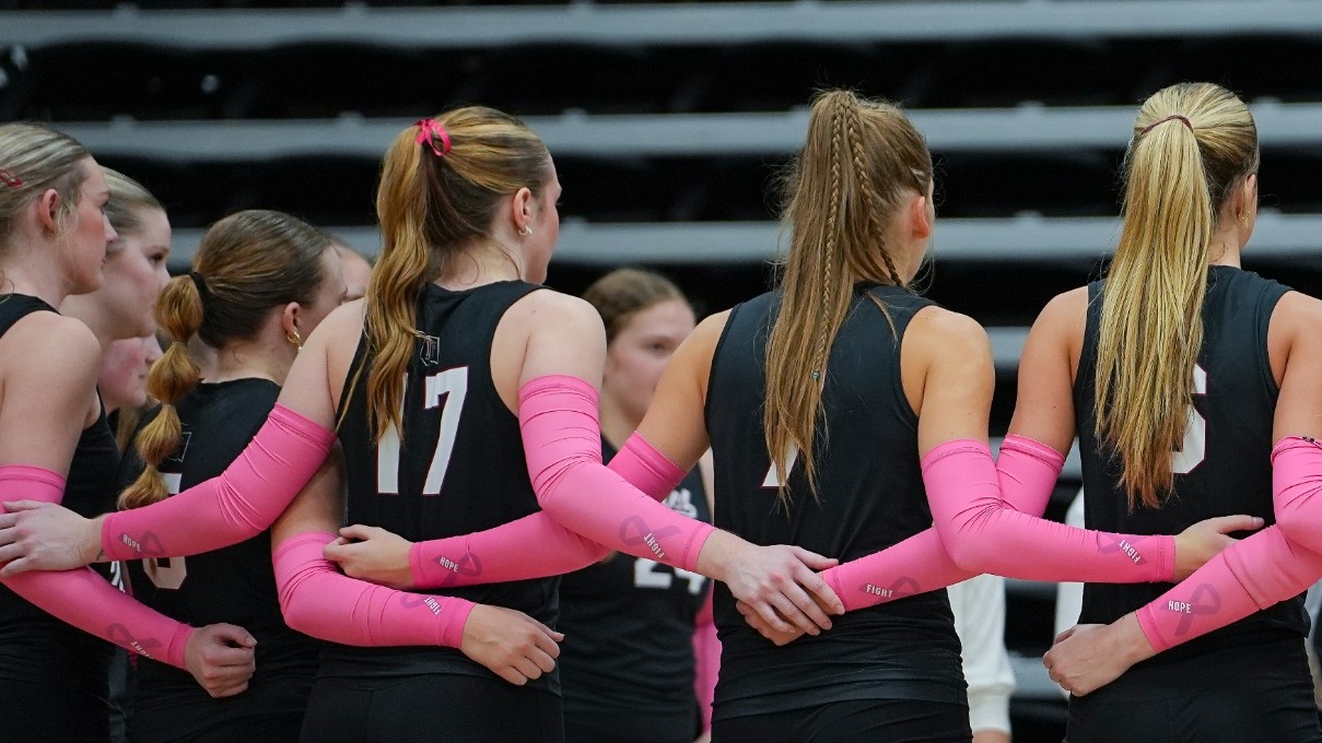 Eagles Volleyball Huddles During a Timeout Against Midwestern State wearing black uniforms with pink arm sleeves