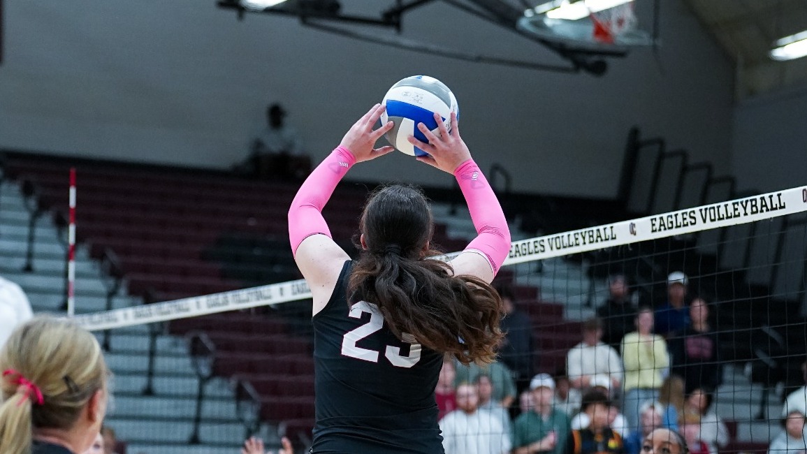 An Oklahoma Christian University volleyball player (No. 23, Emma Eyster) jumps in the air with extended pink arm sleeves to set the volleyball during a match against Midwestern State at the Payne Athletic Center.