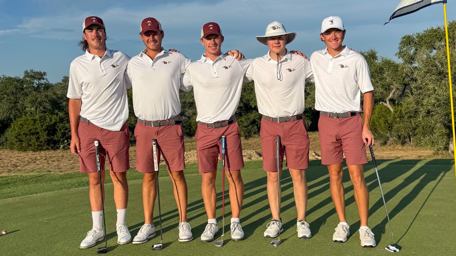 Men's Golf at Dewsweeper - team photo on the green featuring the five competitors, wearing white polos with red shorts, standing on a green.