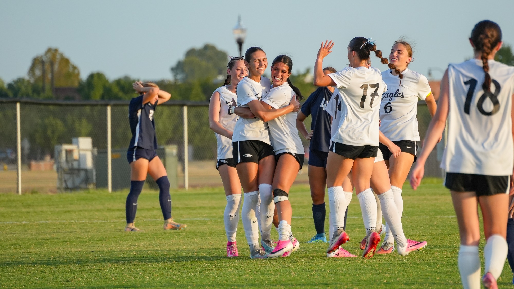 Women's Soccer Gathers to Celebrate Jenna Munson's Goal Against St. Edward's, Wearing White Jersey with Black text and Black Shorts