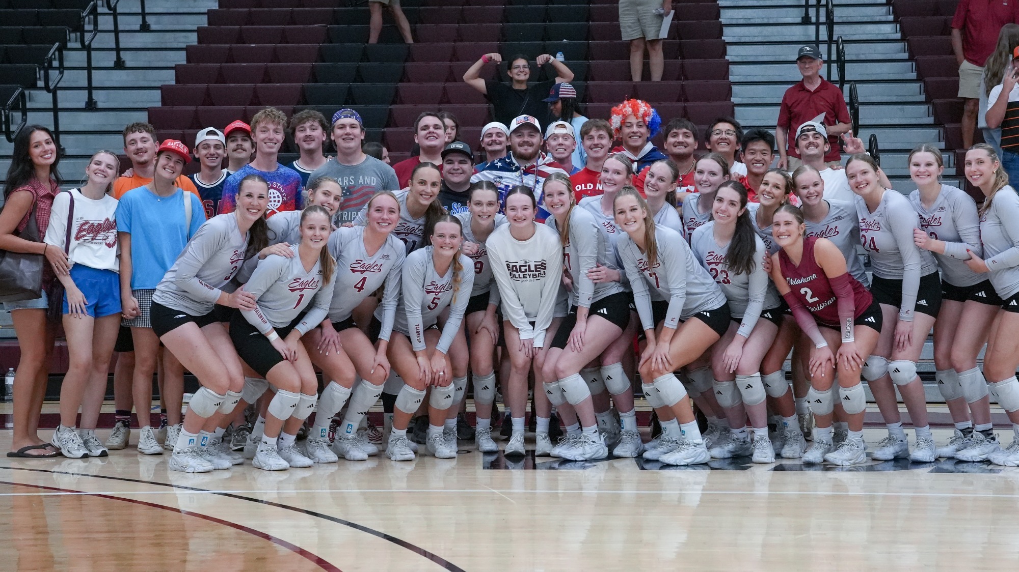 Eagles Volleyball Poses After First Win Against UT Tyler with the Student Section in red, white, and blue attire
