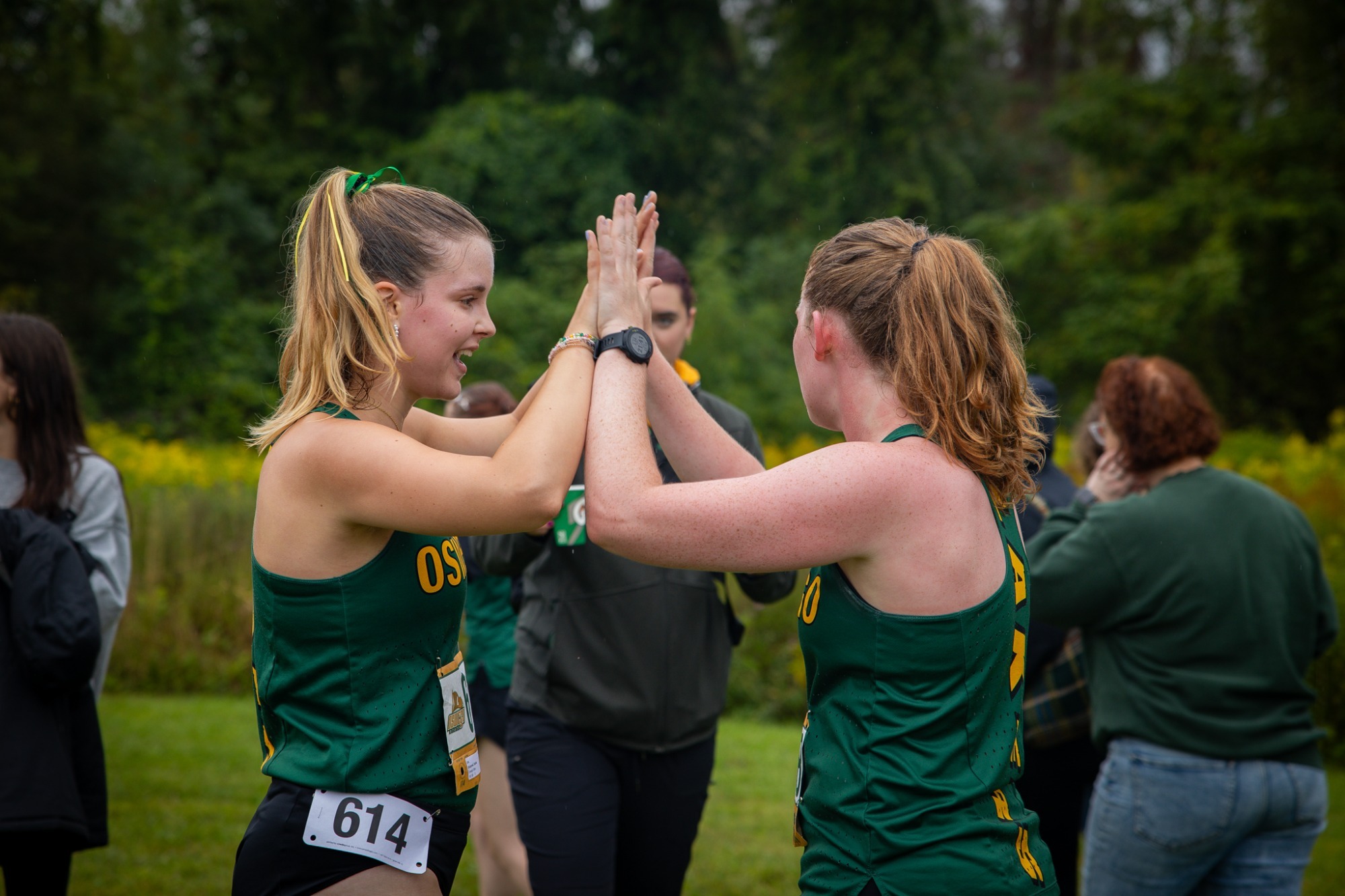 Two cross country runners high fiving after crossing the finish line