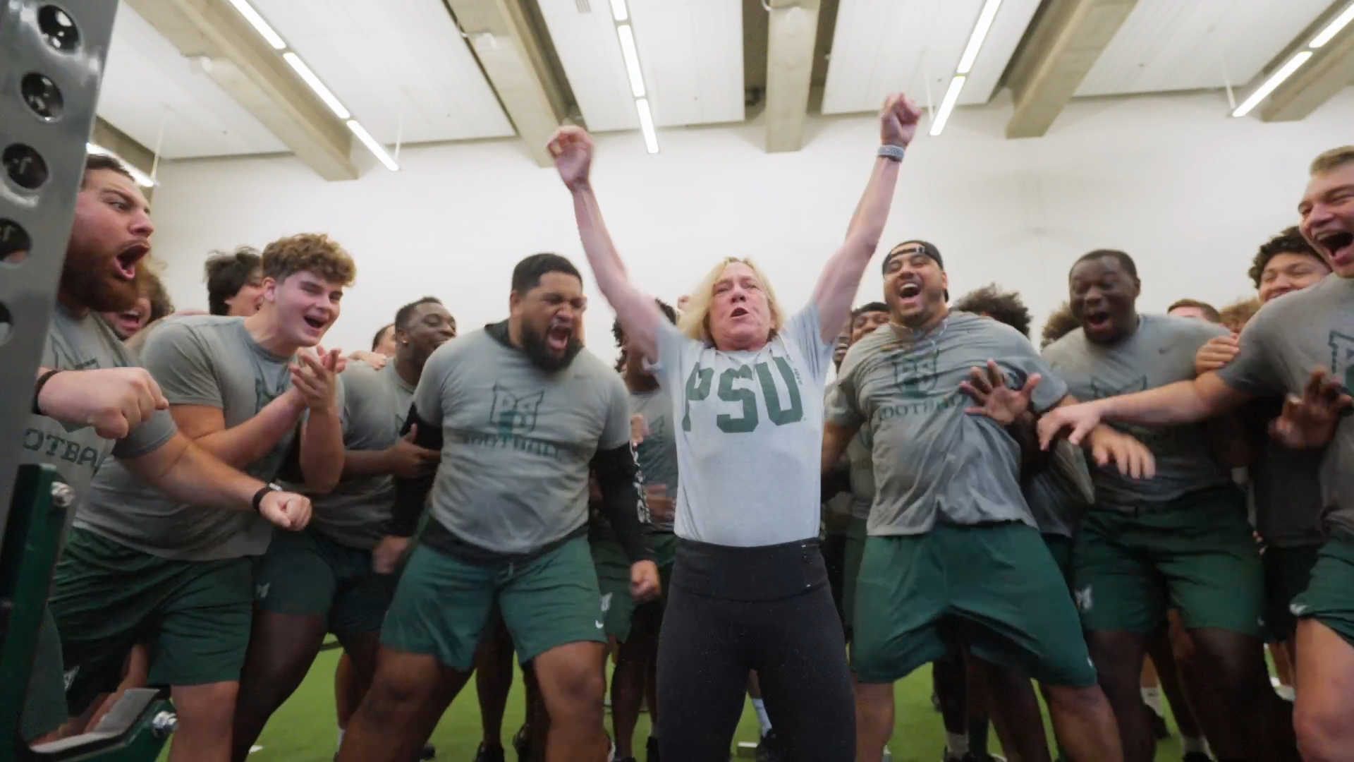 President Ann Cudd celebrates her deadlift with the Portland State football team behind her