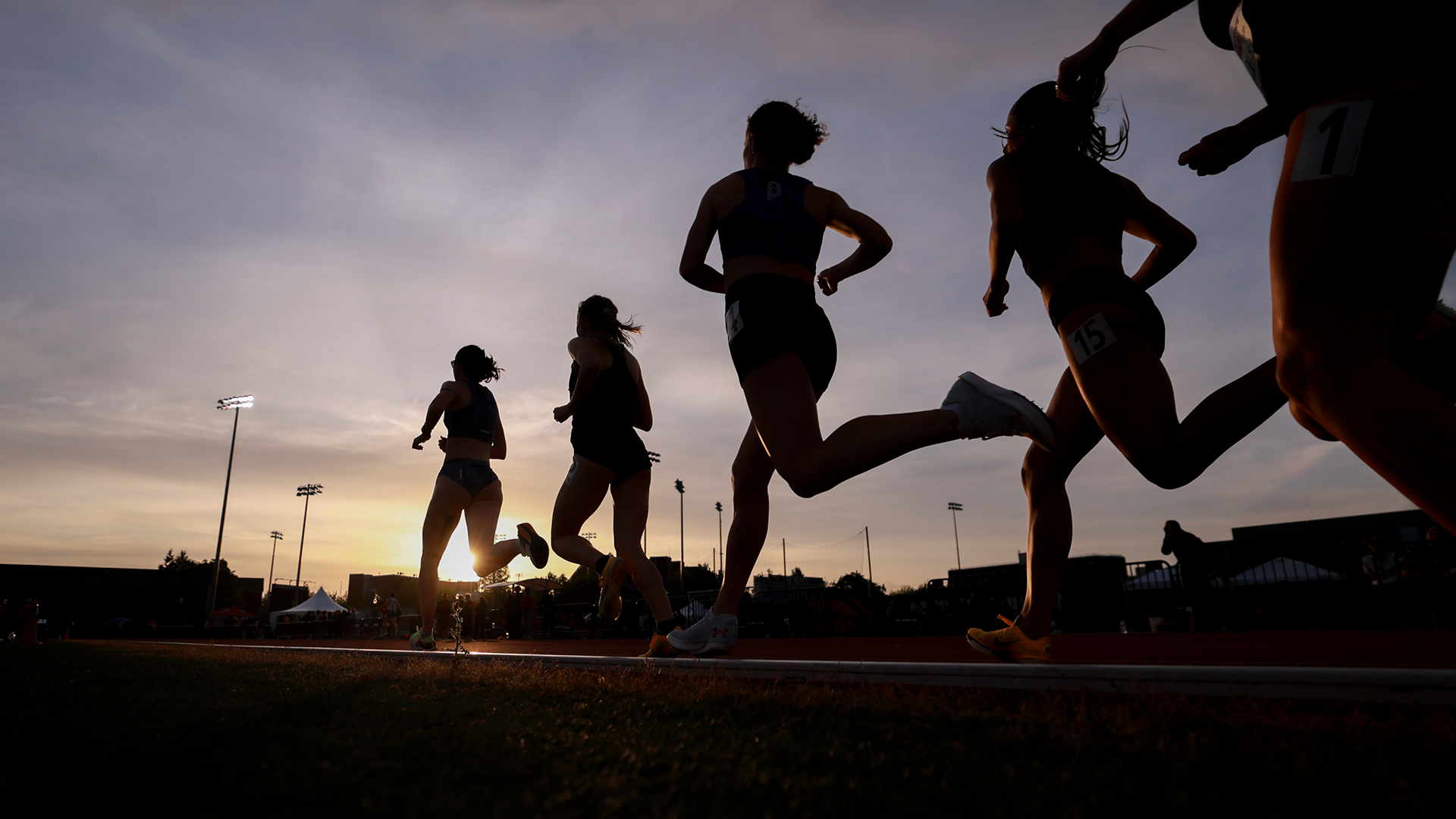 The sun set in the background as 4-5 runners competing at the OSU High Performance Meet compete in a distance event.